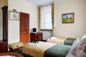 Habitación de hotel con dos camas, un escritorio con computadora, un radiador y una ventana con cortinas florales.
