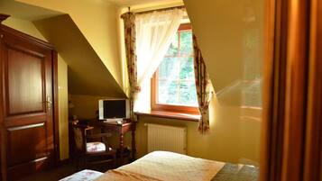 A bedroom with a bed, a desk with a computer, a chair, and a wardrobe.
