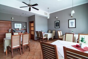A dining area with wooden chairs and tables, a ceiling fan, and wall-mounted light fixtures. - Zajazd Magnolia Airport Modlin (Pomiechowek)