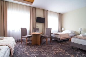 Una habitación de hotel con una cama, dos sillas, una mesita, un televisor y una lámpara.