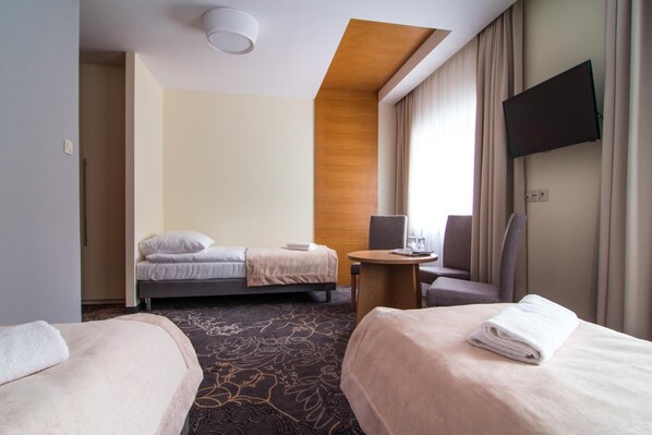 Een hotelkamer met twee bedden, een bureau, een stoel, een televisie en een raam met gordijnen.
