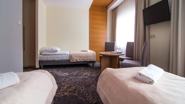Habitación de hotel con dos camas, un escritorio, una silla, un televisor y una ventana con cortinas.