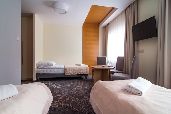 Quarto de hotel com duas camas, uma escrivaninha, uma cadeira, televisão e janela com cortinas.