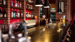 Zona de bar con estantes llenos de botellas de licores, una barra y dos lámparas colgantes.