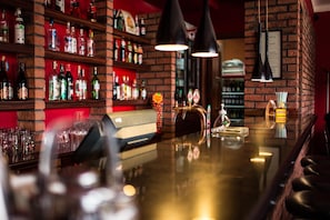 Uma área de bar com prateleiras cheias de garrafas de bebidas, um balcão e duas luminárias pendentes.