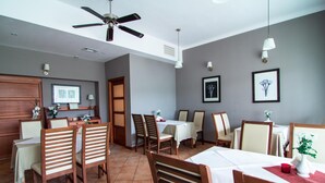 Un comedor con sillas y mesas de madera, un ventilador de techo y lámparas fijadas a la pared.