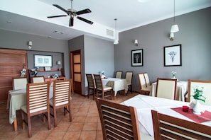 Uma sala de jantar com cadeiras e mesas de madeira, um ventilador de teto e luminárias fixadas na parede.