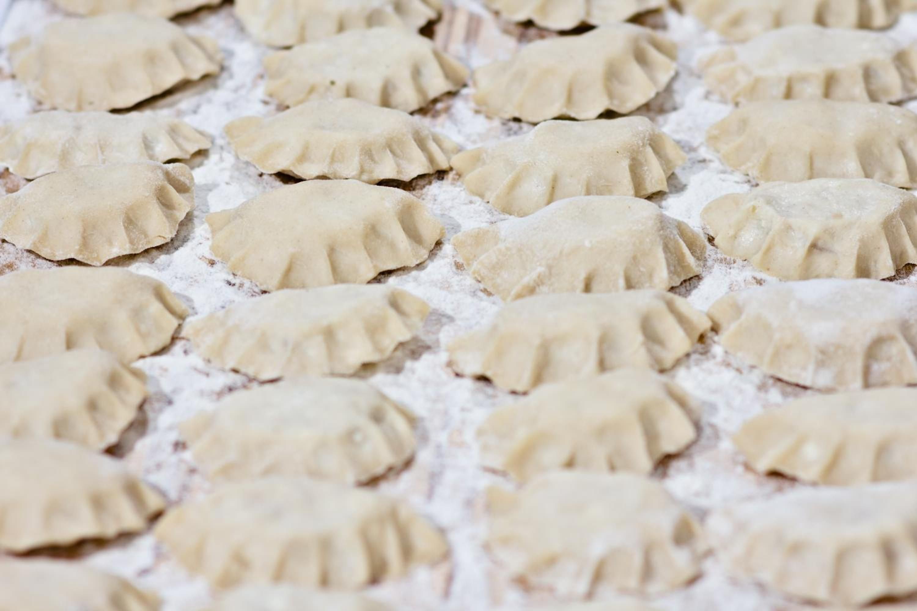 A pattern of uniformly shaped, unfilled dough pieces on a surface dusted with flour.