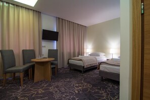 Habitación de hotel con cama, dos sillas, una mesita, televisor y piso alfombrado.