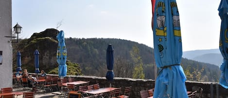 Un área de estar al aire libre con mesas, sillas, sombrillas y vistas a un paisaje montañoso.