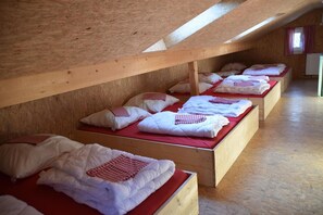 A row of wooden bunk beds with red bedding and white pillows in a room with wooden walls and slanted ceilings. - Naturfreundehaus Veilbronn (Heiligenstadt in Oberfranken)