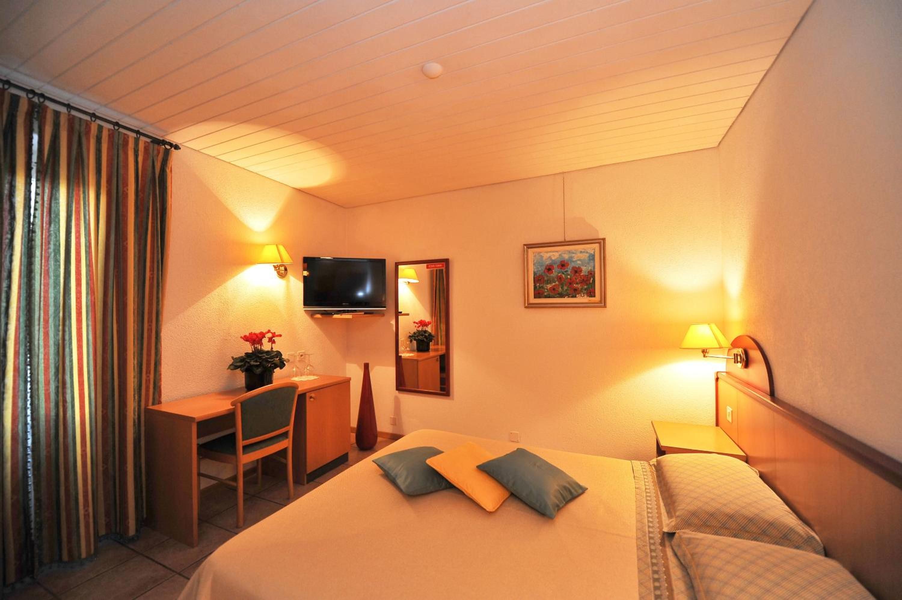 A hotel room with a bed, a desk, a chair, a television, and a painting on the wall.