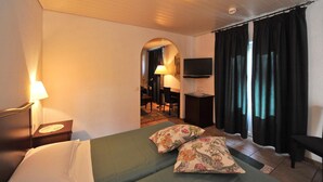 A hotel room with a bed, two pillows, a desk with a lamp, a television, and a window with curtains. - Hotel Ristorante Grotto Serta (Lamone)