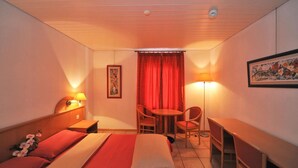 A hotel room with a bed, a desk, a chair, a lamp, and a painting on the wall. - Hotel Ristorante Grotto Serta (Lamone)