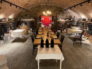 Una bodega con una larga mesa dispuesta para cenar, rodeada de estanterías llenas de vino.