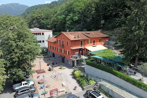 Un hotel con fachada roja, un patio con mesas al aire libre y un estacionamiento.