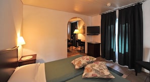 Habitación de hotel con una cama, dos almohadas, un escritorio con lámpara, televisor y ventana con cortinas.