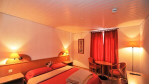 A hotel room with a bed, bedside tables, a desk, a chair, a table, and a window with curtains. - Hotel Ristorante Grotto Serta (Lamone)