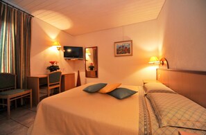 Una habitación de hotel con cama, escritorio, silla, televisión y un cuadro en la pared.