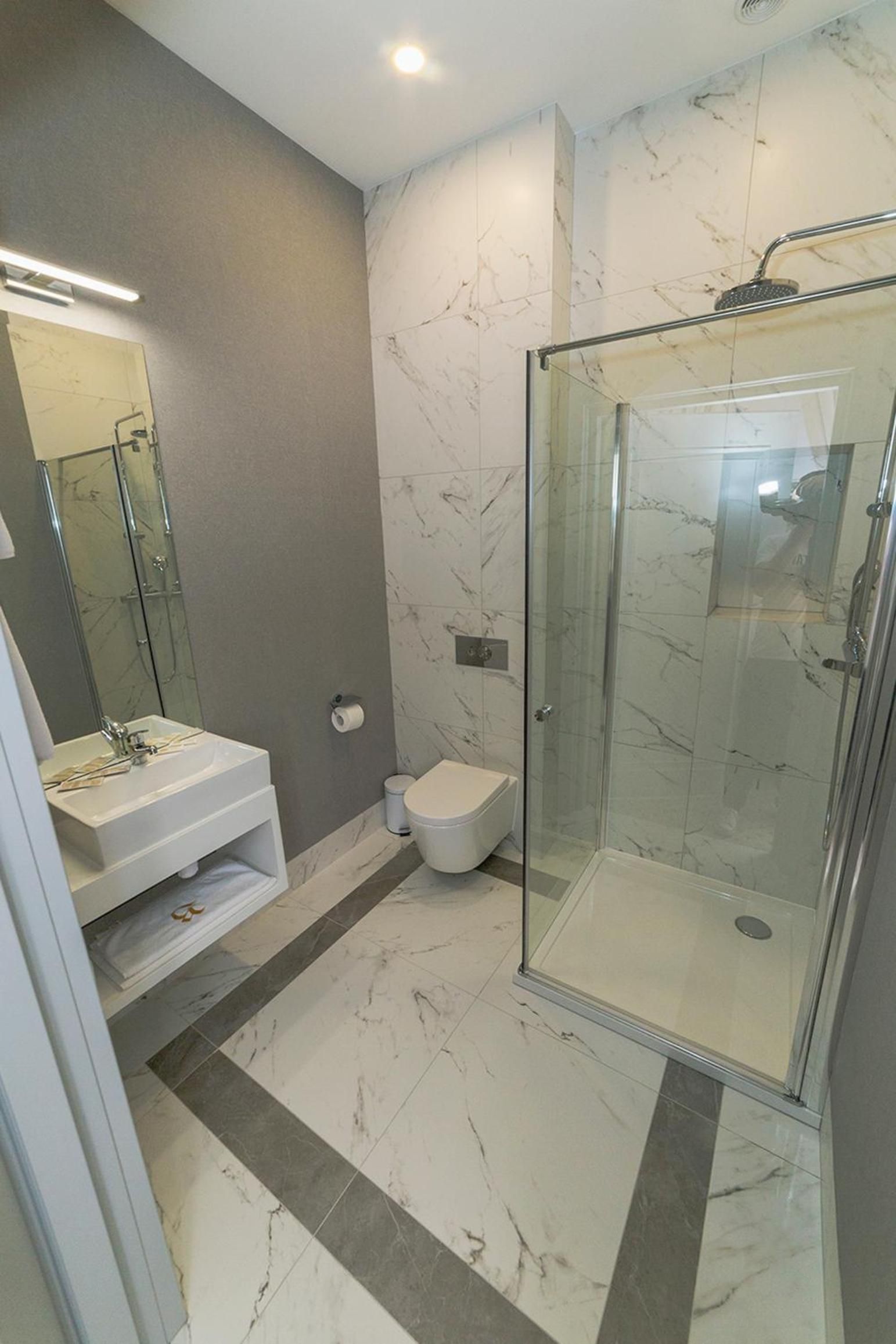 A modern bathroom with a glass-enclosed shower, a white sink, and a toilet.