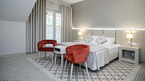 A modern hotel room with a bed, two red chairs, a small table, and a nightstand with lamps.