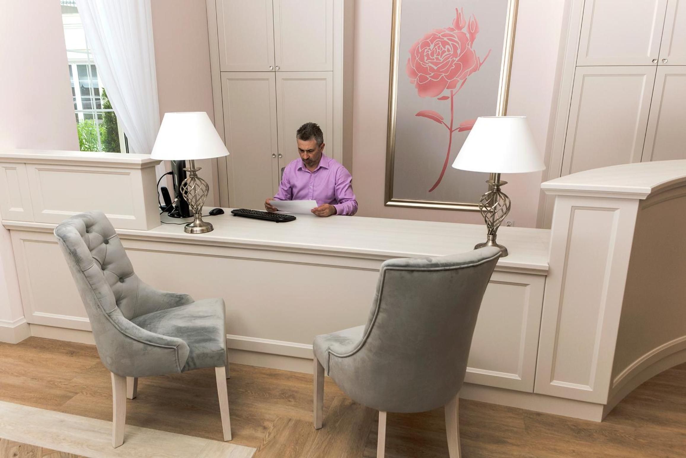 Una recepción con una persona sentada, una butaca tapizada de gris y una obra de arte floral enmarcada en la pared.