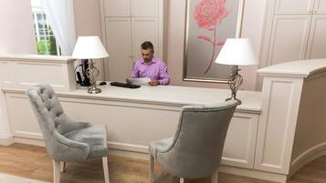 Una recepción con una persona sentada, una butaca tapizada de gris y una obra de arte floral enmarcada en la pared.