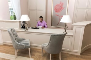 A reception desk with a person seated, a grey upholstered chair, and a framed floral artwork on the wall.