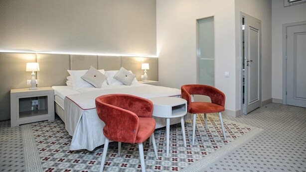 A hotel room with a bed, two bedside lamps, a small table, two chairs, a mirror, and a door.