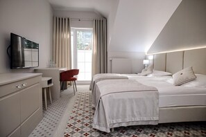 Una habitación de hotel con cama, escritorio, silla, televisor y ventana con cortinas.