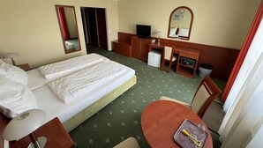 Ein Hotelzimmer mit Bett, Schreibtisch, Stuhl, kleinem Tisch und Spiegel.