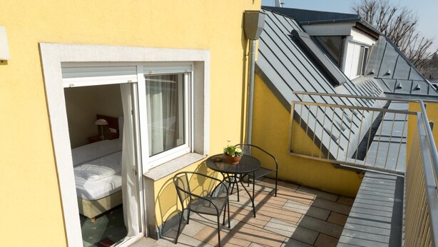 Ein kleiner Balkon mit einem Bett, einem Tisch, Stühlen und einem Blumentopf.