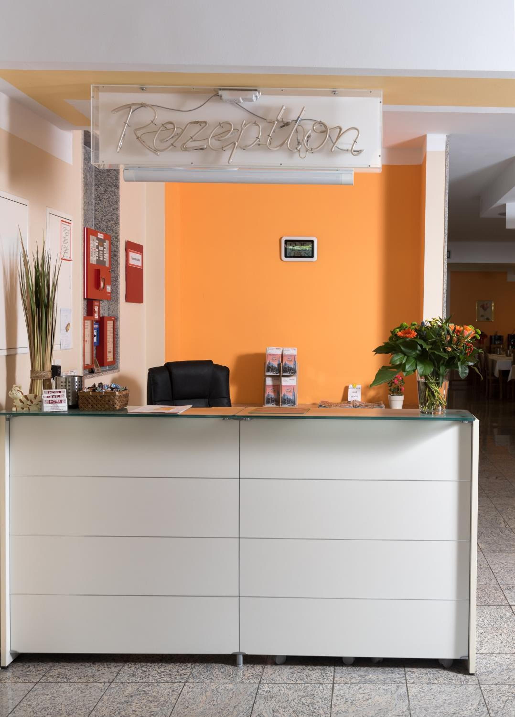 A reception desk with a sign above it, a black chair, a potted plant, and a bulletin board with notices.