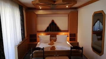 Ein Hotelzimmer mit einem Bett, zwei Stühlen, einem kleinen Tisch, einem Spiegel und einem Fenster mit Vorhängen.