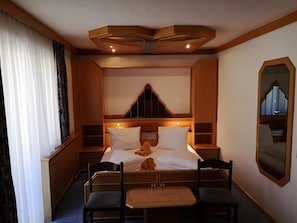 A hotel room with a bed, two chairs, a small table, a mirror, and a window with curtains. - Hotel Thier (Mönichkirchen)