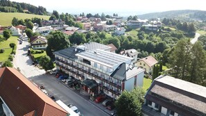 A multi-story hotel with a flat roof and solar panels, located in a residential area with a road and parked cars. - Hotel Thier (Mönichkirchen)