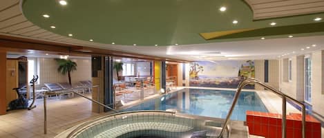 Una piscina interior con un jacuzzi integrado, equipo de ejercicio y un mural con una playa.