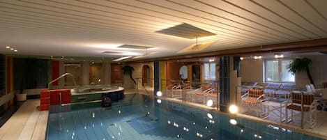 An indoor swimming pool with a tiled floor, lounge chairs, and a hot tub.