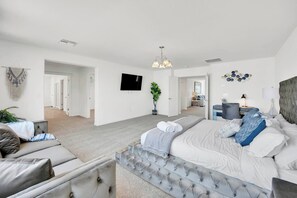 Quarto moderno com cama grande, sofá, televisão e planta.