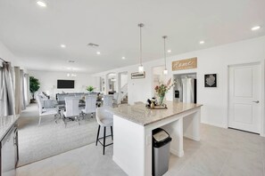 Cozinha moderna com ilha central, sala de jantar com cadeiras e área de estar com sofá.