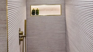 Eine Dusche mit strukturierter Wand, einem goldfarbenen Duschkopf und einem Ablagebrett mit Flaschen.