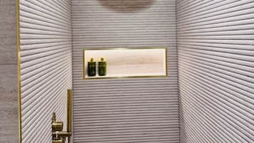 A shower with a textured wall, a gold showerhead, and a shelf with bottles.