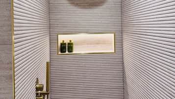 A shower with a textured wall, a gold showerhead, and a shelf with bottles.