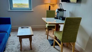 Ein Zimmer mit einer Couch, einem kleinen Tisch, einem Esstisch mit Stühlen, einem Fernseher und einem Fenster mit Blick.