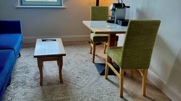 A room with a sofa, a small table, a dining table with chairs, a TV, and a window with a view.