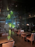 Un espacio interior con paredes de vidrio, mobiliario de mimbre y una mesa central.