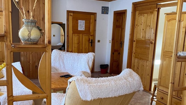A room with a wooden ceiling, a sofa with a white cover, a wooden chair, a wooden cabinet, and a door with a sign. - Family Hotel Markony (Smolyan)