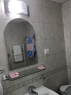 Un baño con pared de azulejos, repisa de vidrio, lavamanos y retrete.