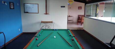 A pool table with balls, a whiteboard with writing, and a window with a view.