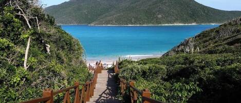 Un escalier en bois mène à une plage d’où l’on a une vue dégagée sur la mer et les montagnes en arrière-plan.